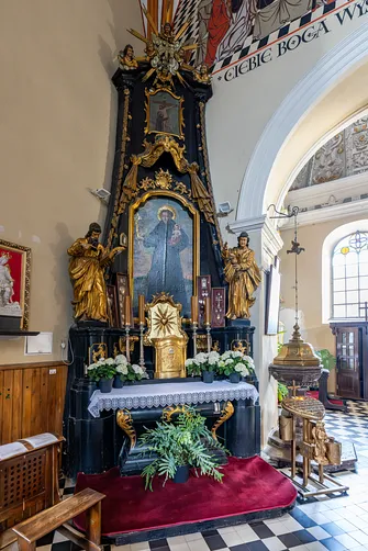 Barokowy ołtarz ze Świętym Antonim i kamienna chrzcielnica w nawie piotrkowskiej fary.