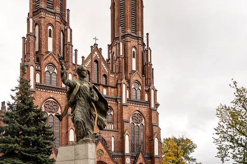 Pomnik ks. Ignacego Skorupki na tle neogotyckiej fasady bazyliki katedralnej św. Michała i św. Floriana w Warszawie.