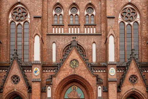 Detal neogotyckiej fasady bazyliki katedralnej św. Michała i św. Floriana w Warszawie z zegarem i oknami.