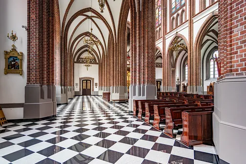 Nawa boczna bazyliki katedralnej św. Michała i św. Floriana w Warszawie z rzędami drewnianych ław.