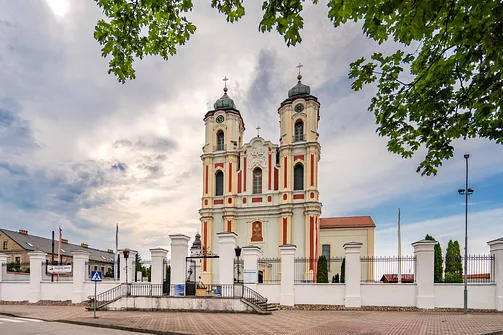 Późnobarokowa fasada bazyliki Nawiedzenia Najświętszej Maryi Panny w Sejnach widoczna zza ogrodzenia.
