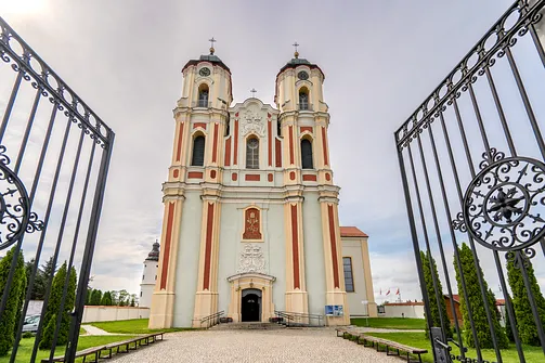 Widok na monumentalną fasadę bazyliki w Sejnach przez otwartą, ozdobną bramę wejściową.