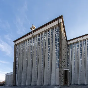 Betonowa fasada świątyni z rzędami pionowych okien i krzyżem w Stalowej Woli.