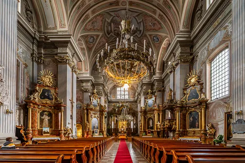 Wnętrze kościoła św. Anny w Warszawie z widokiem przez nawę główną na ołtarz, freski i złocony żyrandol.