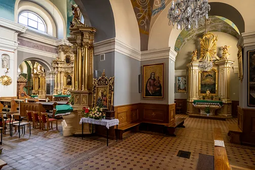 Fragment nawy bocznej rzeszowskiej świątyni farnej z ołtarzami, ławkami i ozdobnym żyrandolem kryształowym.