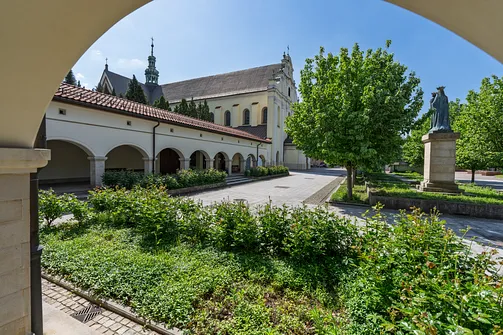 Widok z krużganków na zielony wirydarz, figurę Matki Bożej oraz bryłę mogilskiej bazyliki.