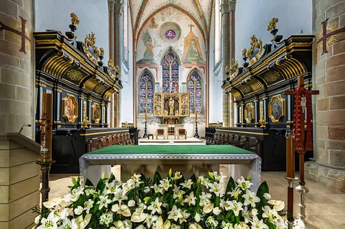 Widok przez współczesny ołtarz posoborowy na zabytkowe stalle i retabulum w prezbiterium.
