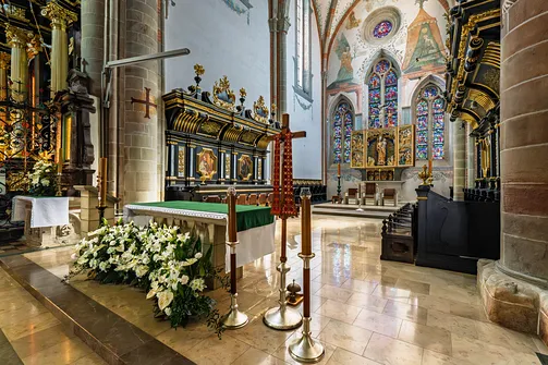 Prezbiterium mogilskiego kościoła z ołtarzem posoborowym, czarnymi stallami i gotyckim tryptykiem w tle.