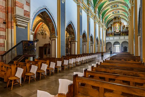 Perspektywa nawy głównej kościoła, ukazująca rzędy ławek oraz prospekt organowy na emporze w głębi.