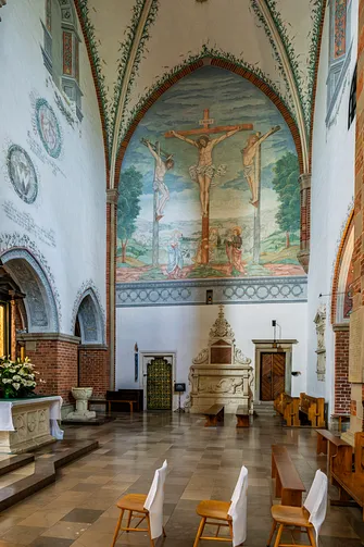 Fragment transeptu z jasnym wnętrzem, ławkami oraz freskiem przedstawiającym scenę Ukrzyżowania.