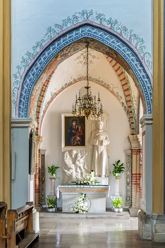 Ołtarz boczny umieszczony w niszy pod ostrołukową arkadą, ozdobiony obrazem Matki Bożej.