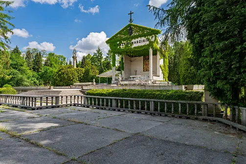 Zadaszony ołtarz polowy w ogrodzie klasztornym, gęsto porośnięty bluszczem z napisem na froncie.