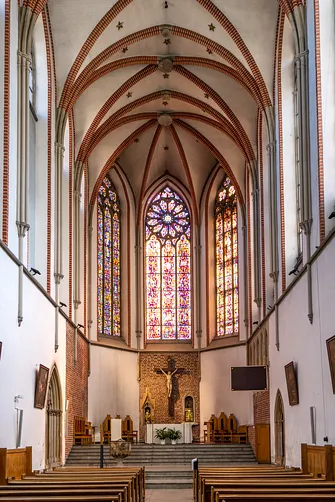 Prezbiterium kościoła św. Wojciecha we Wrocławiu z monumentalnymi, barwnymi witrażami i dużym krucyfiksem.