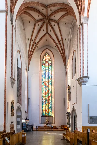 Wnętrze jednej z naw wrocławskiego kościoła z wysokim, barwnym witrażem i gwieździstym sklepieniem.
