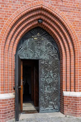 Ostrołukowy portal wejściowy do opolskiej świątyni z ozdobnymi drzwiami.
