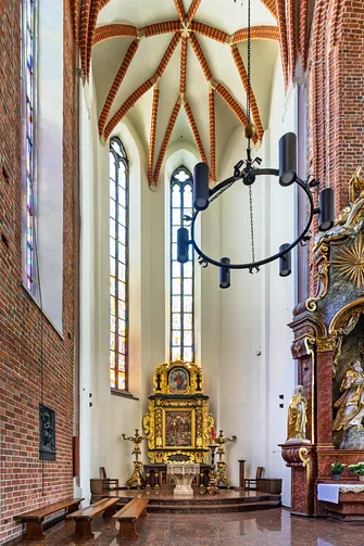 Kaplica z widocznym w głębi złotym ołtarzem, kamienną chrzcielnicą oraz nowoczesnym, kolistym żyrandolem.