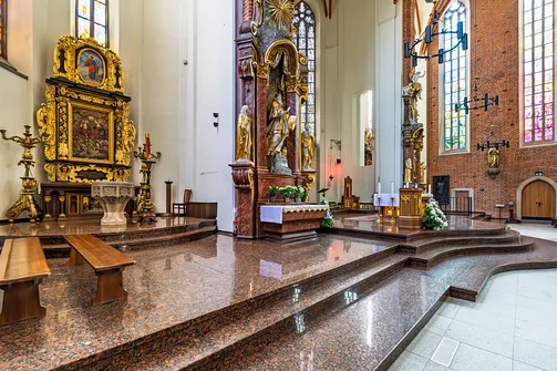 Widok na lśniącą, granitową posadzkę przed podwyższeniem ołtarzowym oraz zabytkowe elementy wyposażenia.