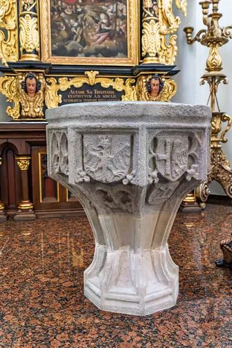 Kamienna chrzcielnica gotycka z rzeźbionymi herbami w prezbiterium opolskiej świątyni.