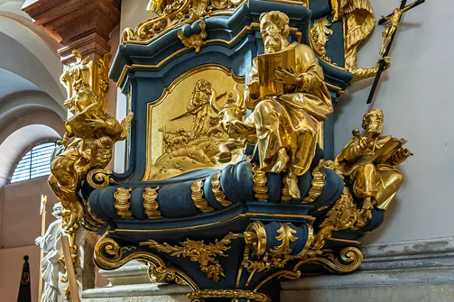 Złocone reliefy i figury ewangelistów zdobiące korpus ambony miechowskiej świątyni.
