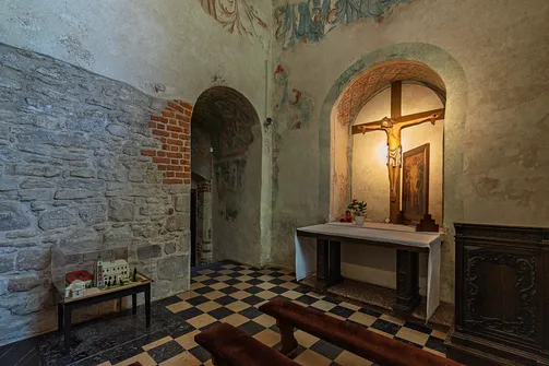 Kaplica z ołtarzem i wiekowym krzyżem na tle surowych, kamienno-ceglanych ścian.