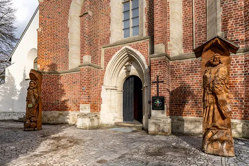 Gotycki portal zachodni kościoła św. Władysława w Szydłowie oraz rzeźby przy wejściu.