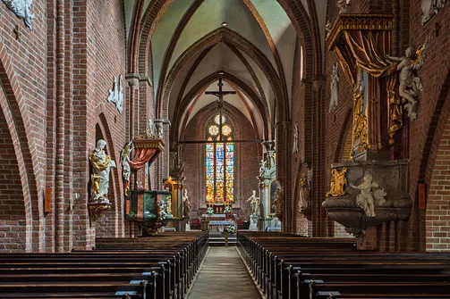 Oś widokowa na prezbiterium sanktuarium w Rudach z dużym oknem witrażowym i wiszącym krucyfiksem.