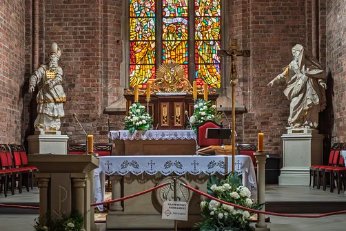 Detal ołtarza głównego z tabernakulum oraz rzeźbami Aarona i Mojżesza na tle barwnego witraża.