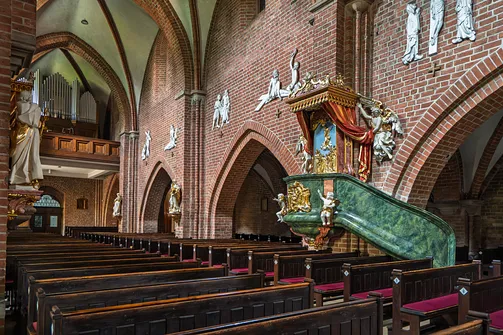 Widok z nawy na schody ambony, ceglane arkady i drewnianą emporę organową rudzkiej bazyliki.