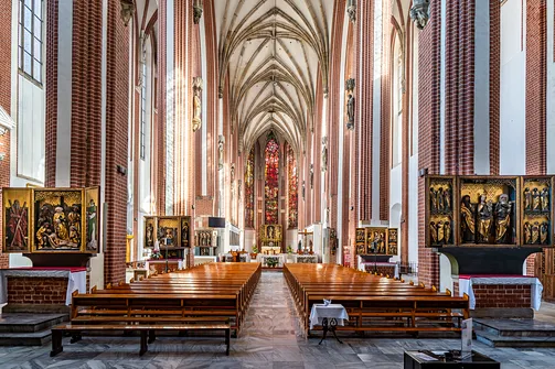 Wnętrze świątyni na Piasku we Wrocławiu z gotyckimi filarami i ołtarzami bocznymi.