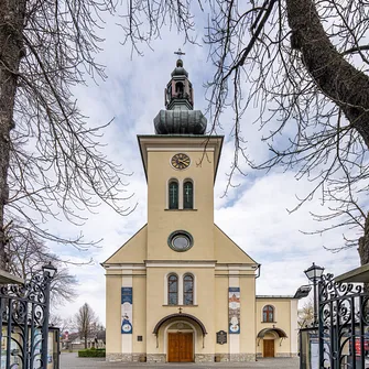 Frontowa elewacja kościoła w Bielsku-Białej z centralną wieżą i kamienną bramą.