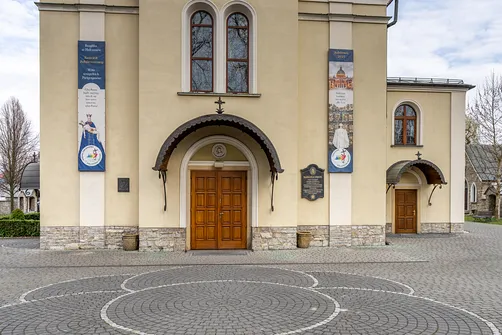 Portal główny bielskiej bazyliki z zadaszeniem i tablicą pamiątkową na elewacji.