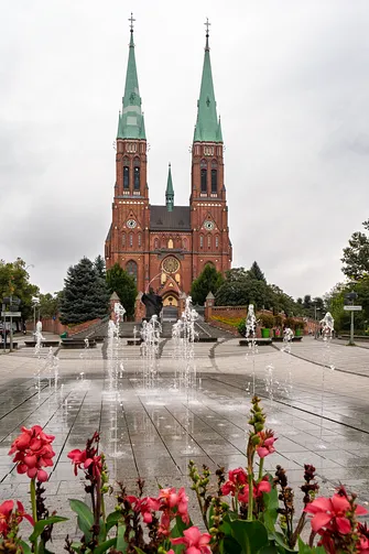 Widok z perspektywy placowej fontanny na neogotycką fasadę rzymskokatolickiej bazyliki w Rybniku.