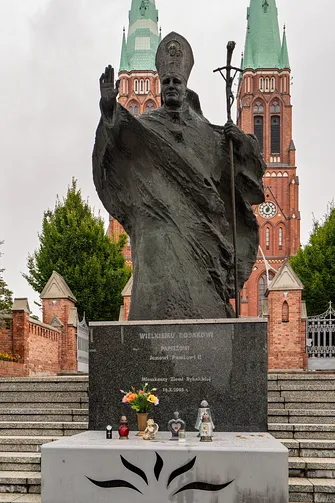 Monumentalny pomnik papieski na tle dwóch strzelistych wież neogotyckiego kościoła w Rybniku.