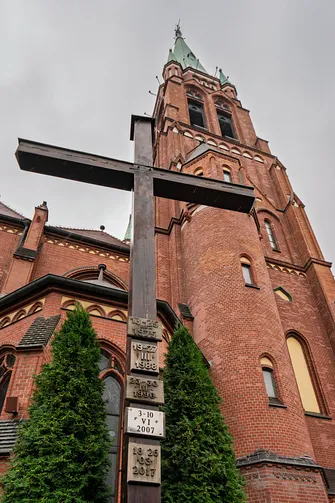 Drewniany krzyż misyjny przy ceglanych murach i wieży bazyliki św. Antoniego w Rybniku.