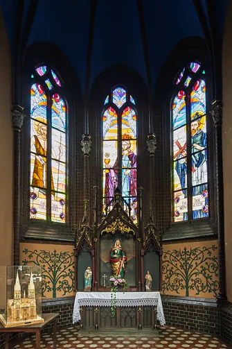 Neogotycki ołtarz boczny na tle barwnych witraży w kaplicy świątyni.