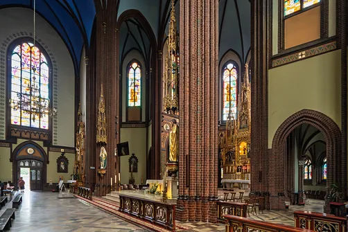 Architektura wnętrza rybnickiej bazyliki z widokiem na kaplice boczne i ceglane filary.