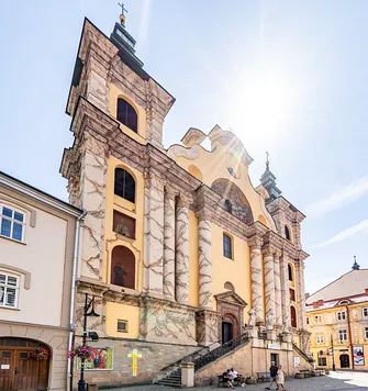 Dwuwieżowa fasada franciszkańskiej świątyni w Przemyślu z kolumnowym portalem i rzeźbami.