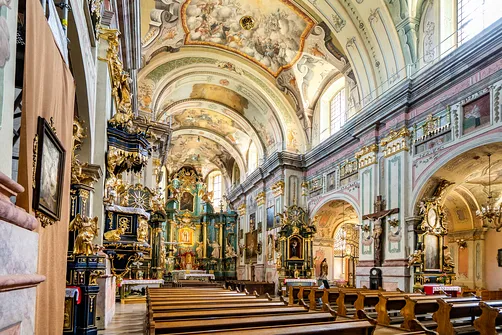 Perspektywa nawy głównej franciszkańskiej świątyni z polichromiami ściennymi i rokokową amboną.