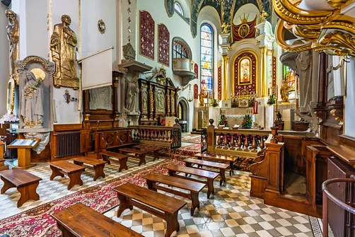 Przestrzeń nawy przed prezbiterium limanowskiego sanktuarium z drewnianymi ławami.