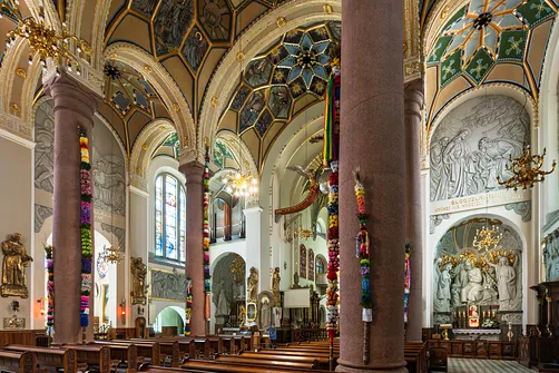 Wnętrze nawy głównej sanktuarium w Limanowej z dekoracyjnymi palmami przy kolumnach.