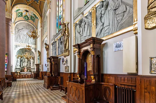 Drewniane konfesjonały oraz płaskorzeźbione stacje Drogi Krzyżowej w nawie bazyliki.