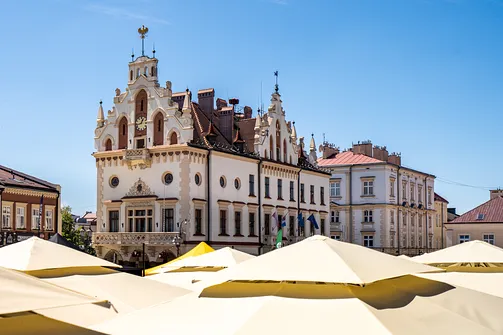 Frontowa elewacja ratusza w Rzeszowie widziana ponad parasolami ogródków.
