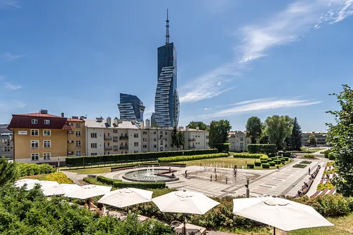 Park miejski z kompleksem fontann na tle nowoczesnego wieżowca Olszynki Park w Rzeszowie.