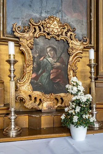 Obraz w rzeźbionej ramie i mosiężne świeczniki na mensie ołtarzowej.